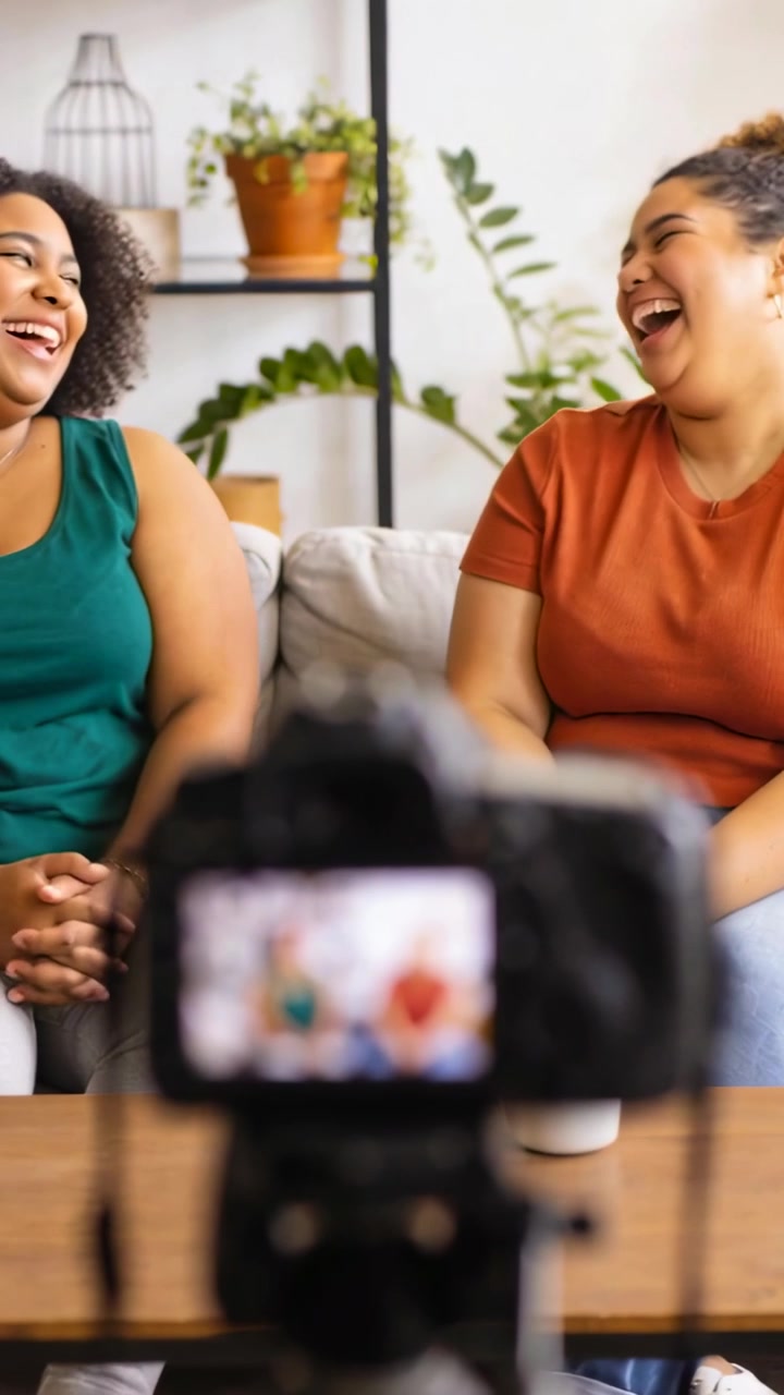 Vertical video: Starting tripod cam, two women in green and rust talking on couch at home for vlog