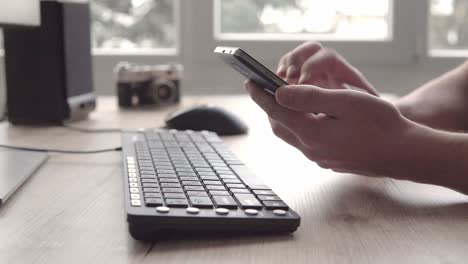 young man using mobile phone smartphone while sitting computer keyboard and mouse. freelancer working and using phone for communication with clients.