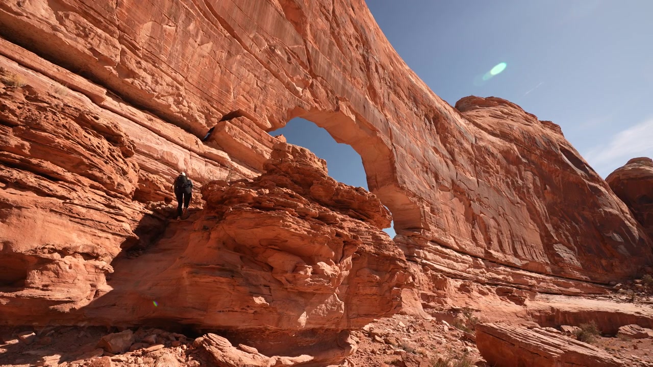 Donna che cammina su roccia sotto Jeep Arch, punto di riferimento naturale panoramico vicino a Moab, Utah, USA