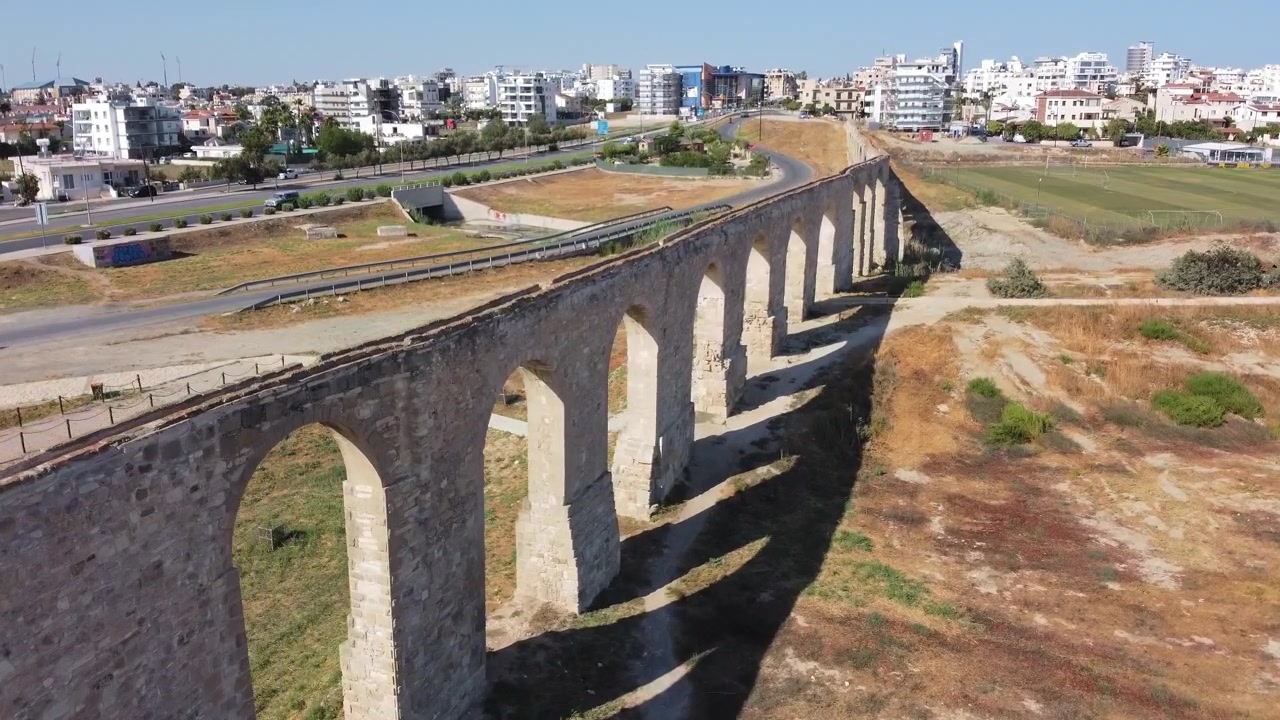 Archi in pietra di una struttura di acquedotto storico con edifici moderni della città e strada sullo sfondo