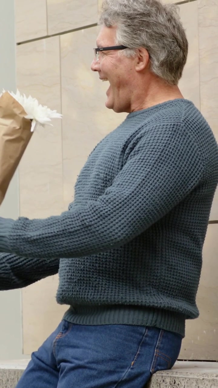 Video verticale: Uomo che avvista una persona, si alza, saluta e porge un bouquet su una sporgenza, con spazio per il testo.
