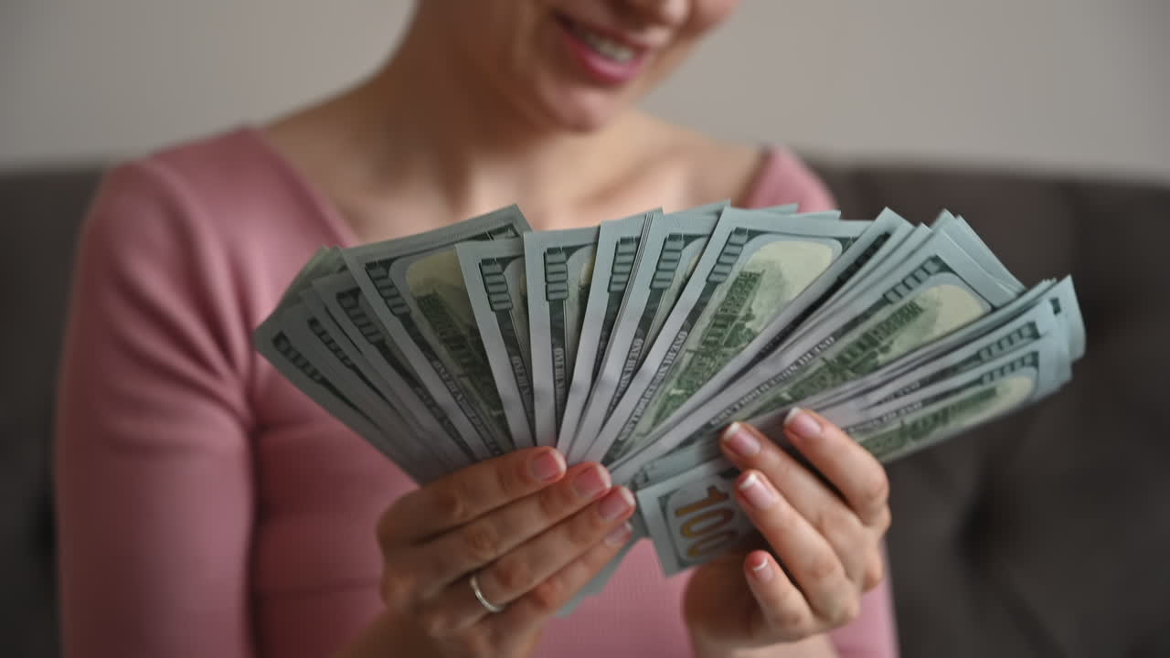 Smiling woman admiring a large fan of one hundred dollar bills in her hands
