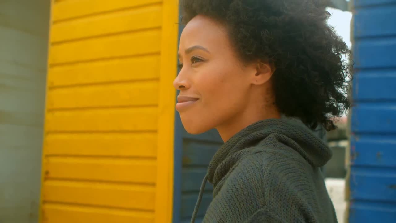 Thoughtful young African American woman walking at beach hut 4k