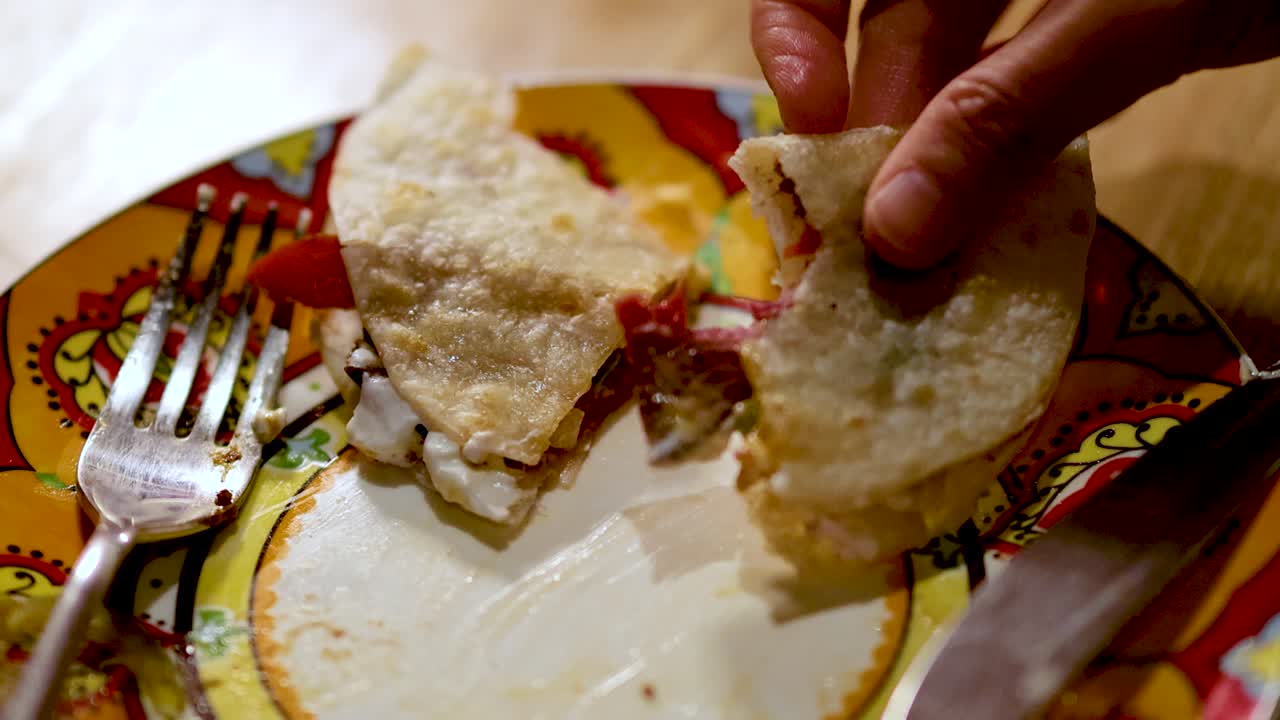 Hand lifts quesadilla from vibrant plate in warmly lit restaurant, close-up, shallow depth of field