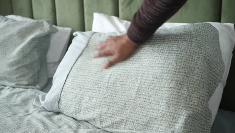 a person's hand reaches for a pillow on a bed