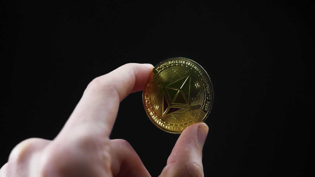 A close-up of a hand shifting a gold Ethereum coin, reflecting under light with black background
