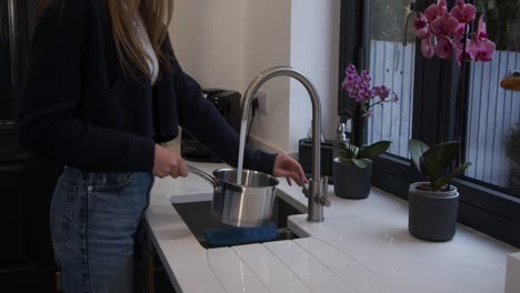 female model tuning on tap filling a pan with water in a kitchen