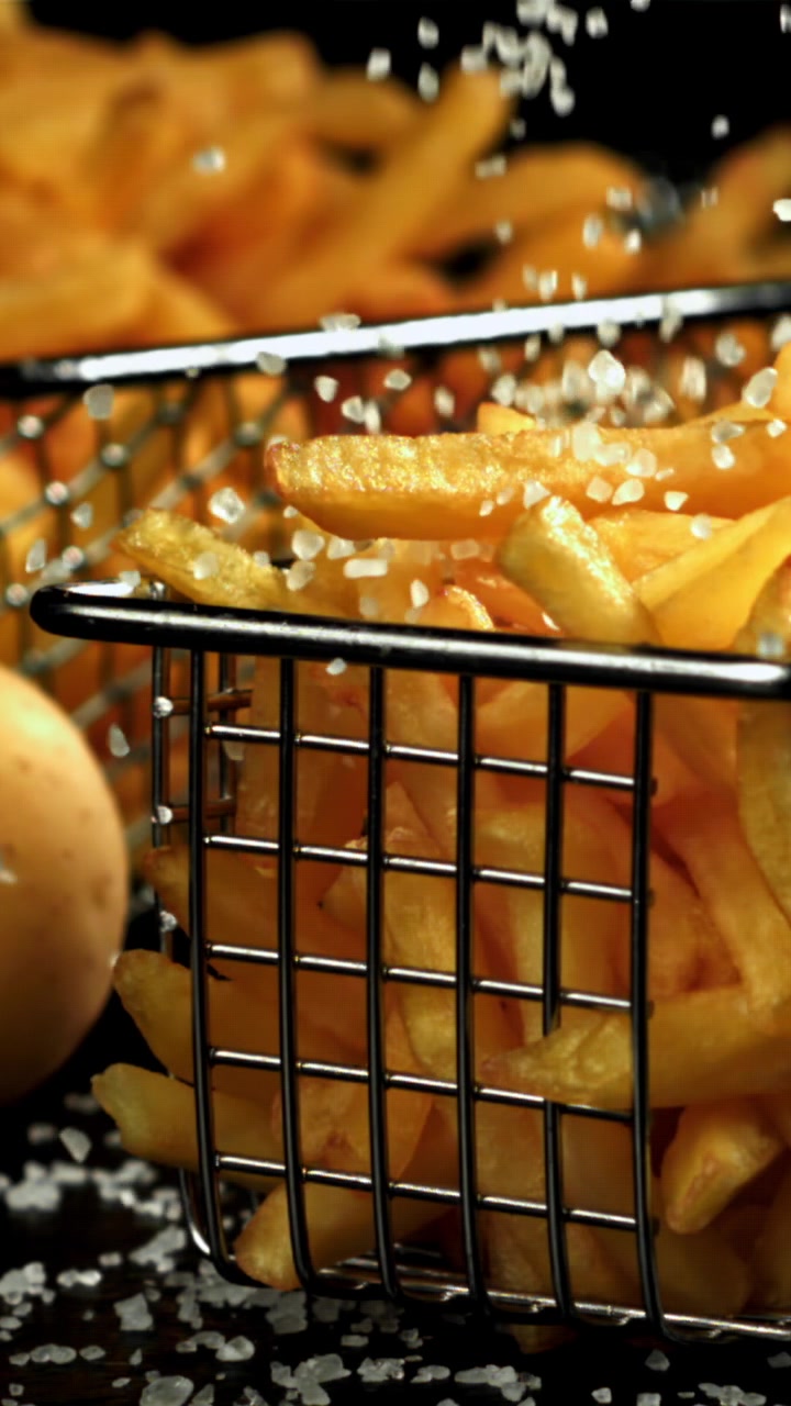 Sal sendo polvilhado em câmera lenta sobre batatas fritas douradas e crocantes