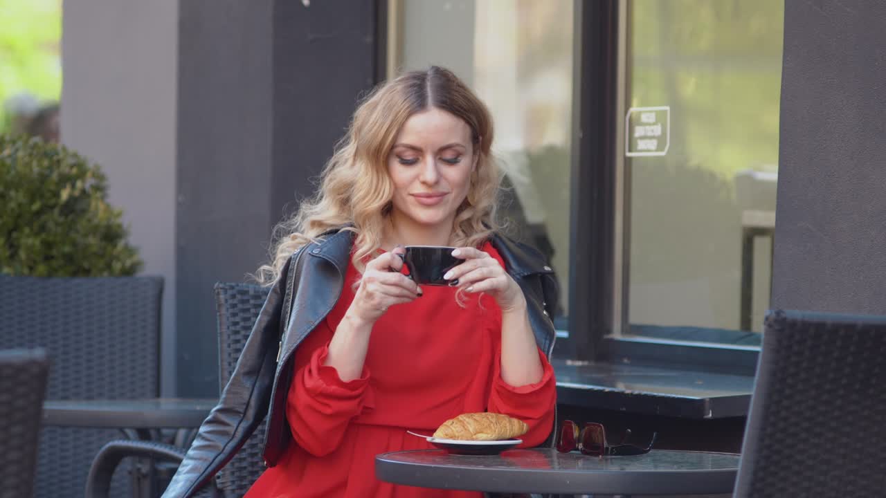 Slow morning drinking coffee. Romantic blonde in a red dress and biker jacket drinks coffee in restaurant's terrace
