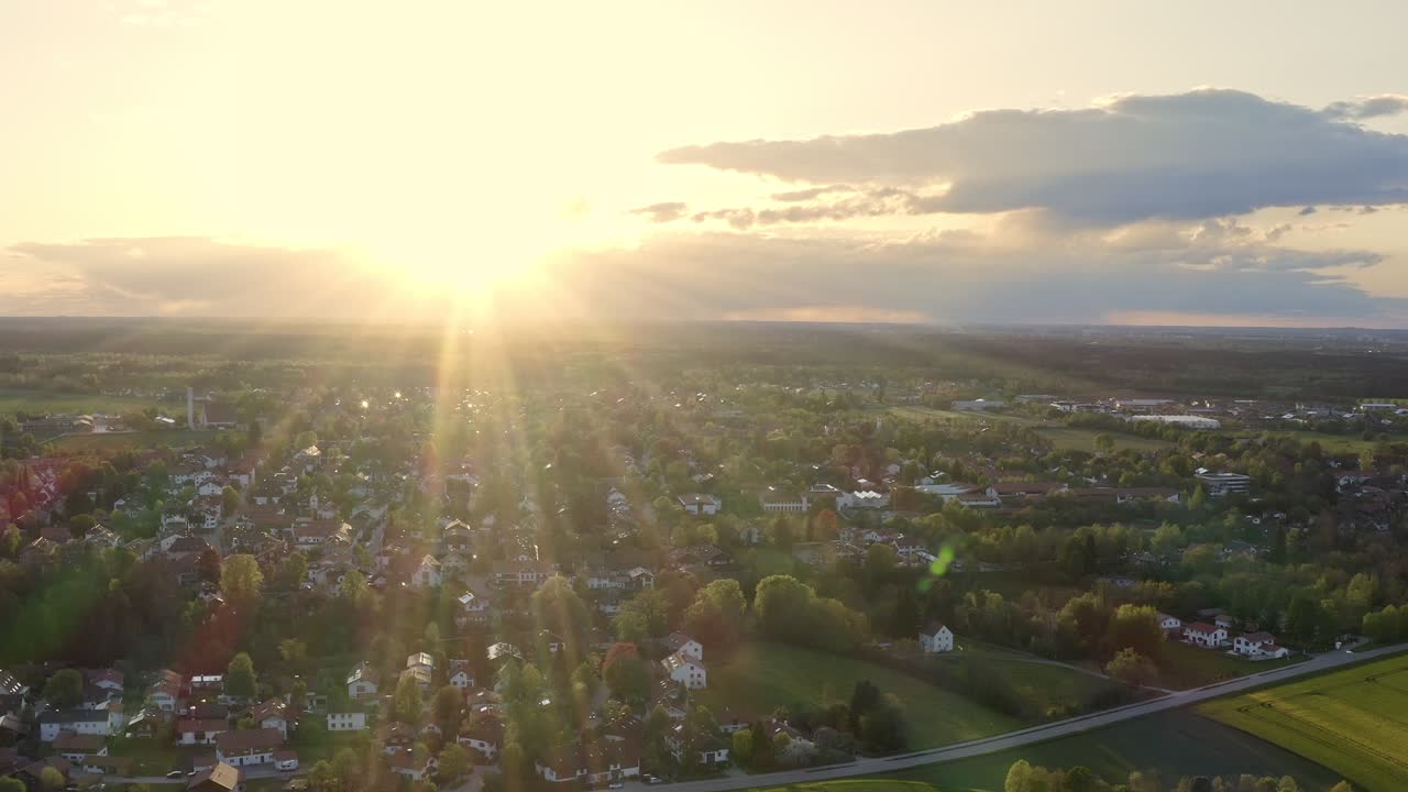 Heller, sonniger Abend nach einem wunderschönen Frühlingstag, Drohnenflug rückwärts über eine Kleinstadt im Sonnenschein mit Wolken am Himmel.