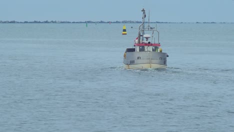 pequeño barco de pesca costero blanco sale del puerto de liepaja, día nublado, pescador listo para pescar en un mar báltico, negocios locales, tiro medio distante