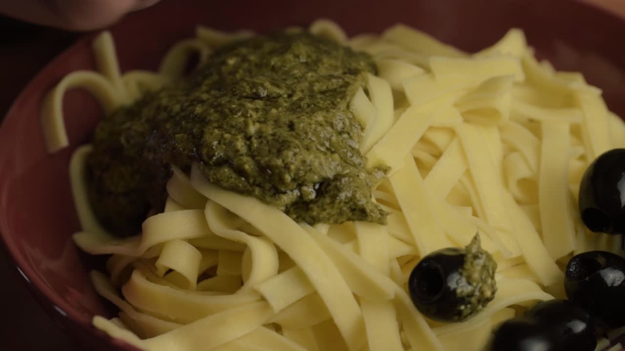 sirviendo pasta tagliatelle con salsa de pesto verde y aceitunas negras en primer plano