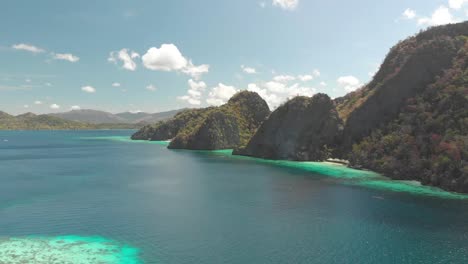 aerial drone shot over turquoise lagoons, and towards limestone cliffs on a paradise isle, on a sunny day, at coron island, philippines, asia