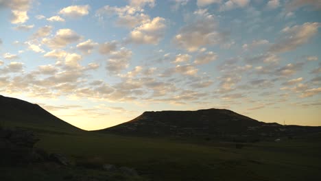 timelapse: early morning, small, softly lit clouds travel across the sky before sunrise, with grassy landscape and sandstone hills slowly lighting up and turning green on a summer morning in lesotho