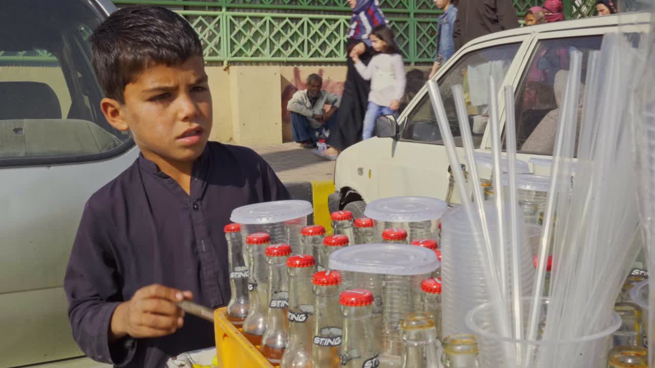 Adorable child street vendor selling glasses of tangy homemade lemon soda from a vibrant cart in a crowded marketplace.
