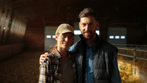 caucasian young couple of farmers looking at camera in a stable with sheep flock