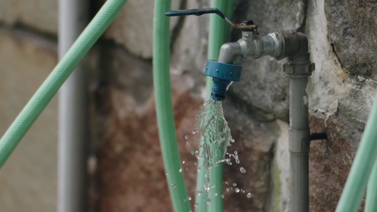 Close up of water flowing from a green hose against a stone wall