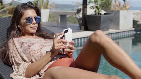 Stylish-woman-using-smartphone-at-poolside