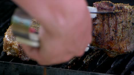 un par de pinzas para carne colocan un jugoso filete de costilla casi cocido en una parrilla y lo deslizan un poco