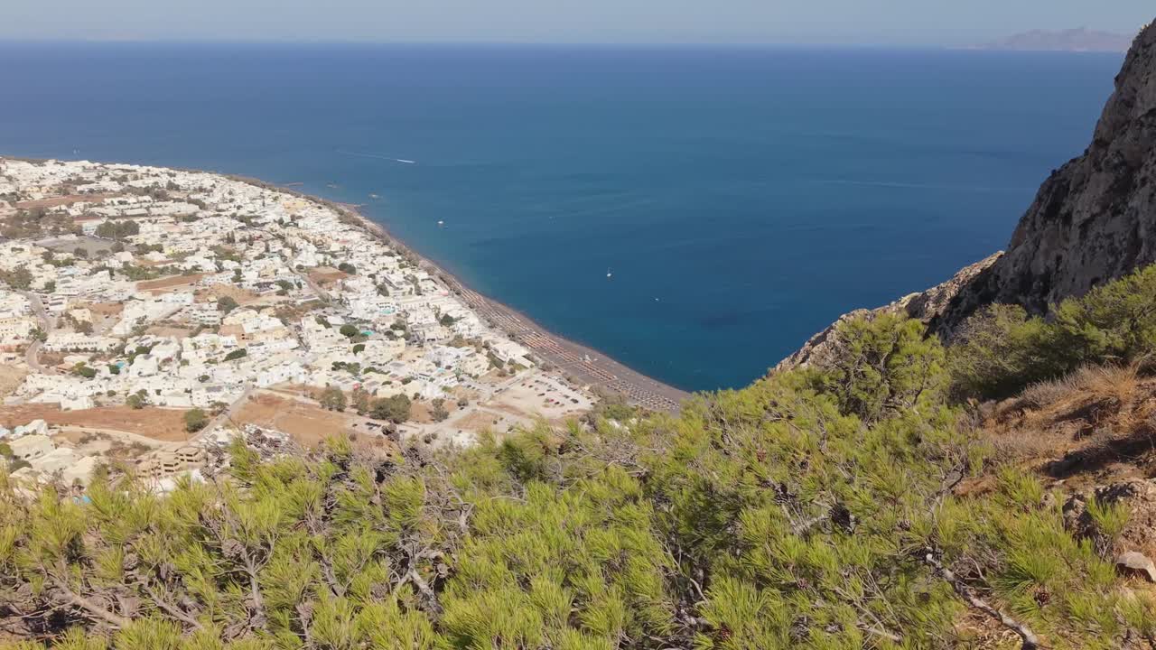 Dron odhalující krajinu Kamari na Santorini, představující pobřeží, útesy kaldery, křišťálově čisté Egejské moře a ikonickou sopečnou ostrovní scenérii