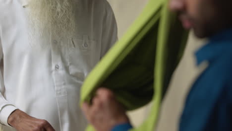 studio shot of two sikh men folding fabric for turban against plain background in real time