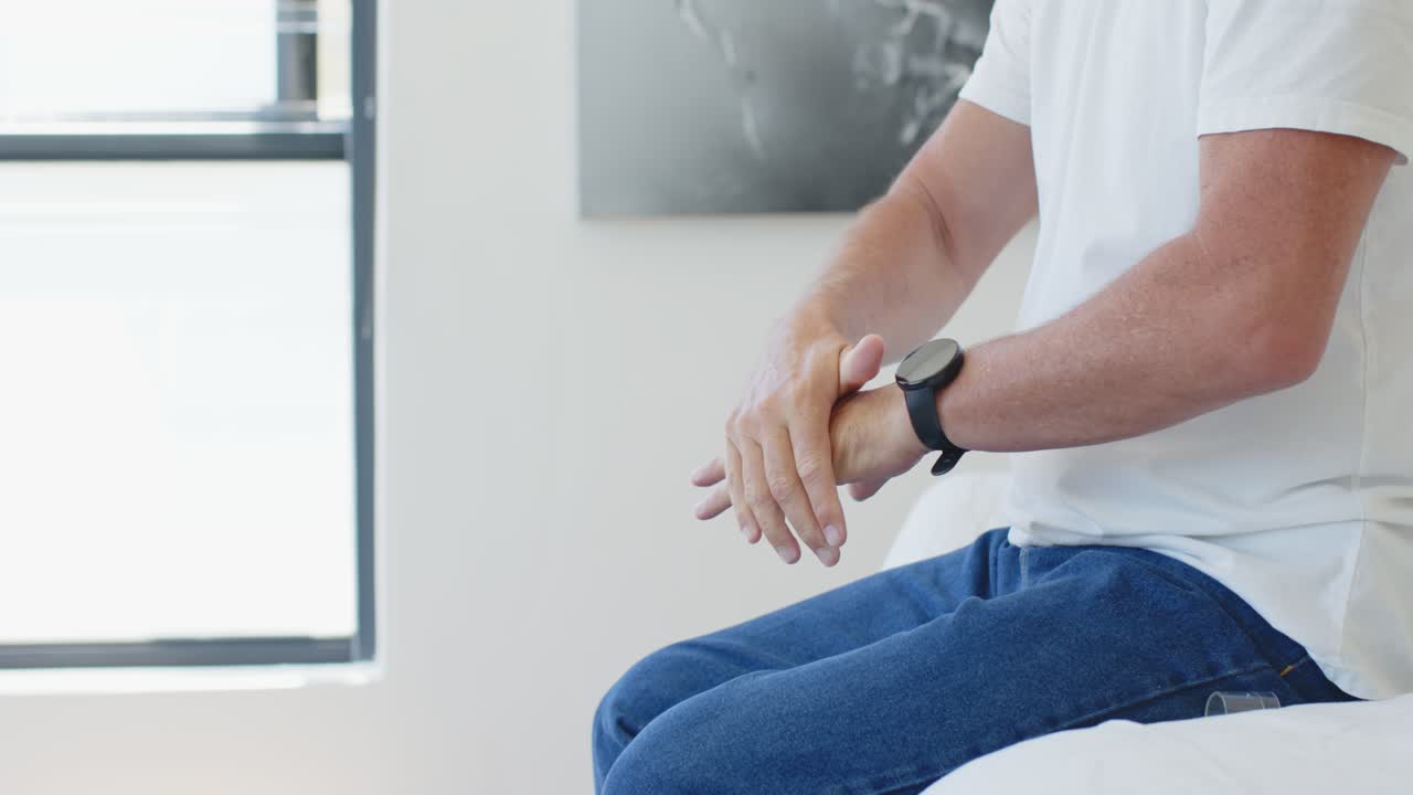 La mano destra si allunga, le mani stanno regolando lo smartwatch sul polso sinistro sul bordo del letto, assicurandosi che sia ben aderente.