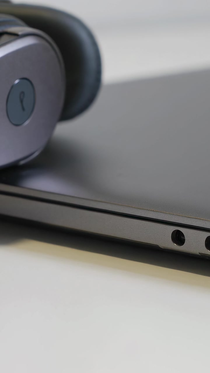 Video verticale: Ripresa che mostra un auricolare wireless appoggiato sul coperchio di un laptop su una scrivania, evidenziando le porte