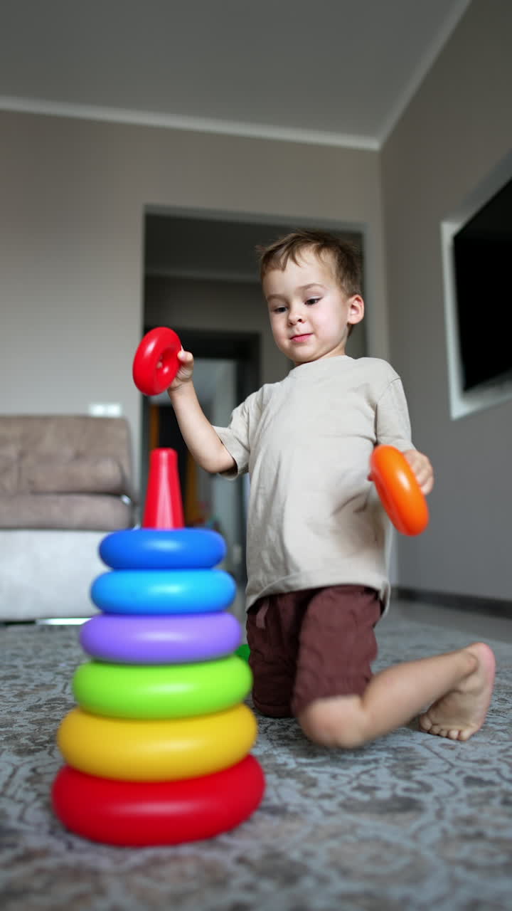 Active Caucasian toddler builds a pyramid. Lovely baby boy plays at home cheerfully. Vertical video.
