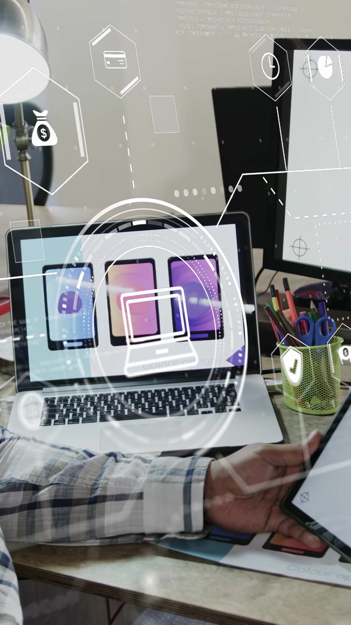 Video vertical: Hombre inclinando una tablet, animando iconos en un anillo HUD sobre un portátil, mostrando el diseño de una aplicación.