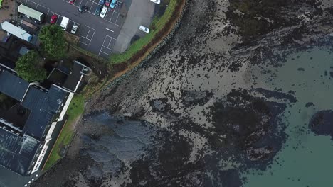 aerial birds eye flyover of a beach with turquoise water, a car park and then a small village