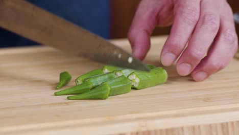 slicing green okra on a wooden cutting board