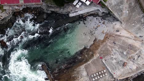 hermanus old harbour from above as swimmers exit the water with large waves crashing against the breakwater