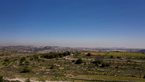 fly over green hills, big white building city in the far background, shot with drone