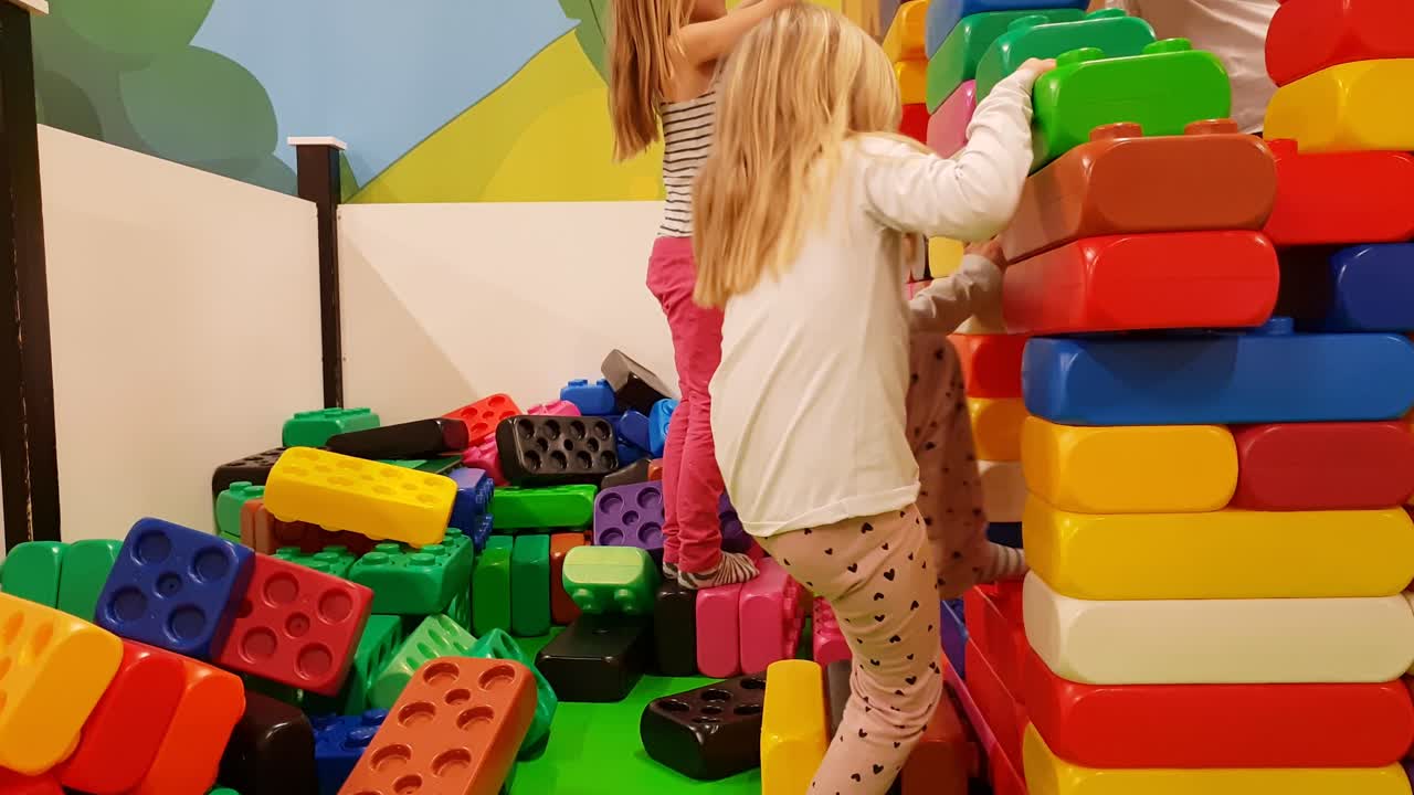 Children building with big Lego bricks blocks at indoor amusement park, failing and ruining Lego house, happy to sad in one second