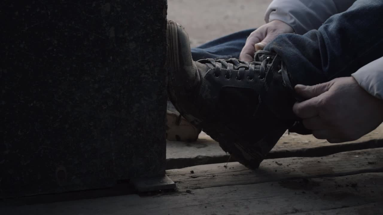 Hiker stops in rustic wooden building barn to tie shoelaces on walking boots medium shot