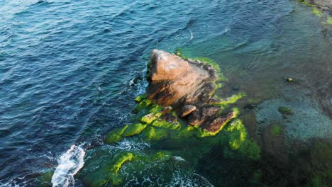 Arc-aerial-shot-around-rock-in-the-sea-at-sunset,-bright-colors