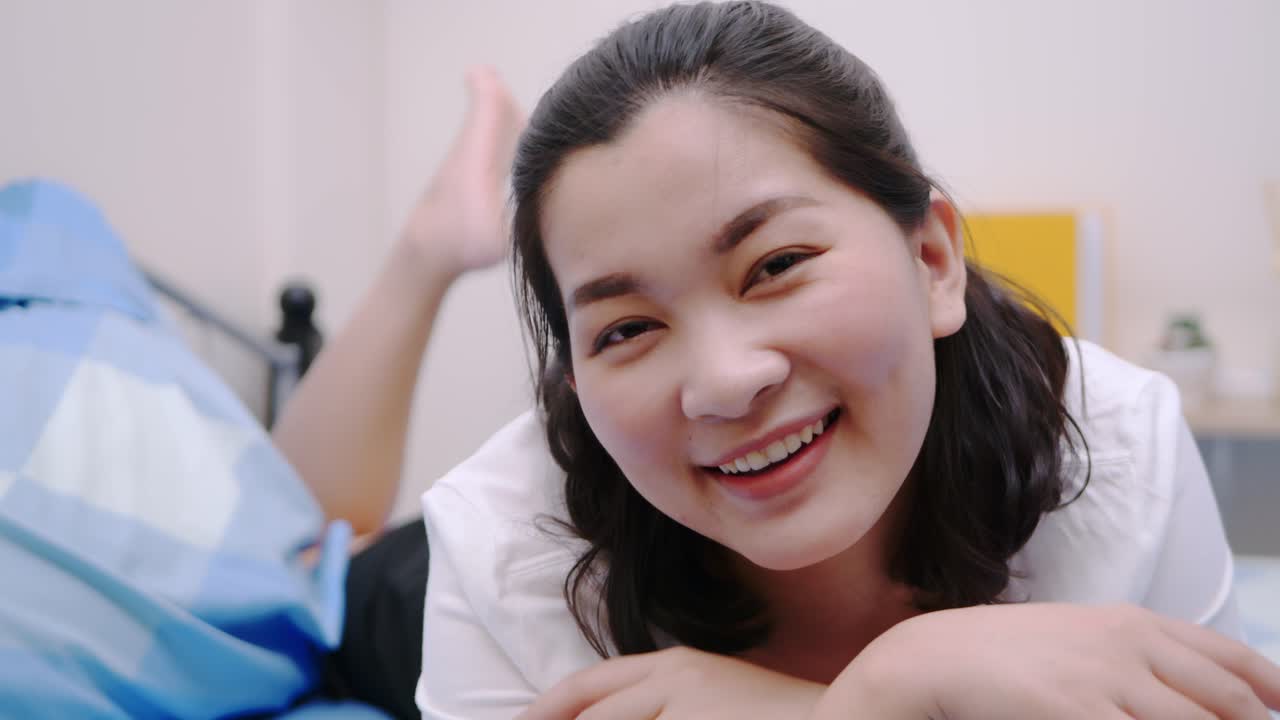 아름답고 웃는 아시아 여성들은 휴일에 침대에 누워 매우 행복하고 만족하며 맑은 빛, 느린 동작의 장면으로 휴식을 취합니다.