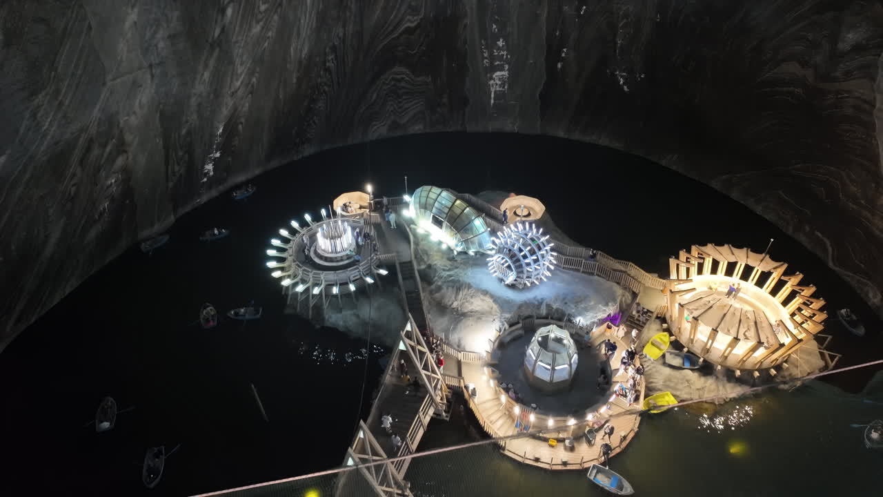 View of the underground Turda salt mine lake with illuminated wooden platforms and modern installations, surrounded by boats