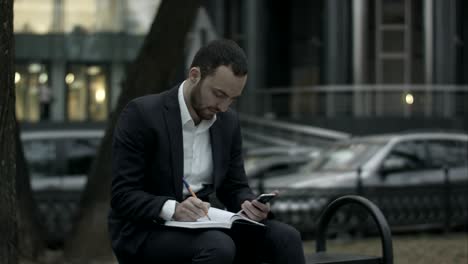 young business man  working with papers and phone at green park, waiting for meetin