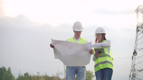 ingenieros de coworking con tabletas en la planta solar. hombres y mujeres adultos con cascos usando tabletas mientras están al aire libre en la plataforma de transformadores. transporte de energía limpia. entrega de energía eólica