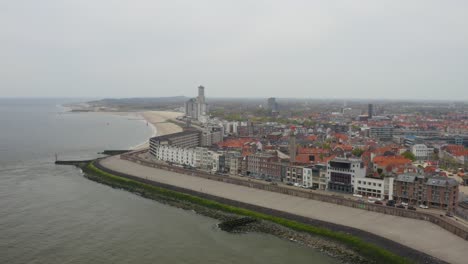 Aerial-descending-orbit-over-the-waterfront-boulevard,-city-beach,-old-fortifications,-and-marina-entrance-in-Vlissingen,-Zeeland,-The-Netherlands