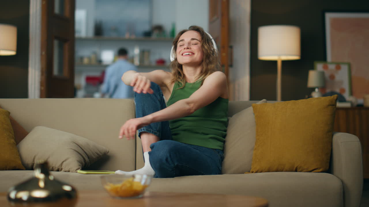 Headset lady listening music smiling sofa. Happy girl enjoying song dancing beat