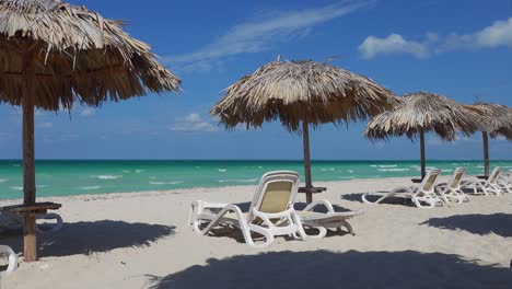 sand beach, straw umbrellas in varadero, cuba, white sunbeds and blue ocean, wind and strong water waves