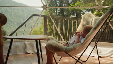 niño pequeño sentado en una silla acogedora frente a la hermana examina cuidadosamente los paisajes montañosos y el bosque fuera de la ventana de glamping. apartamentos de lujo en la naturaleza con montañas para vacaciones familiares