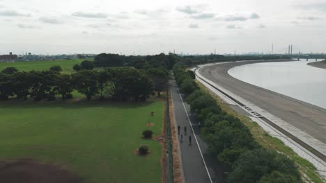 Group-Of-Cyclists-Ride-Bikes-Along-The-Arakawa-River-In-Saitama,-Japan