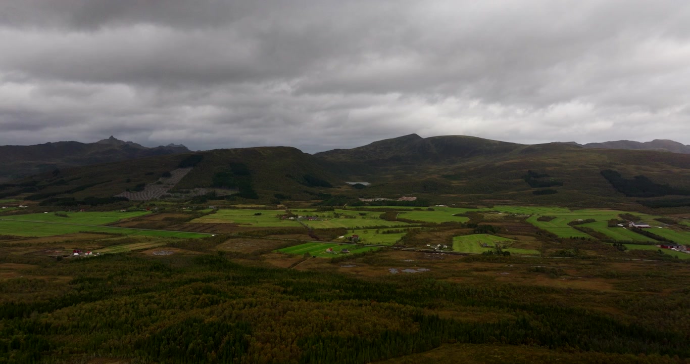 Paesaggio di Sortland, Norvegia settentrionale, con campi verdi lussureggianti e montagne che si ergono in lontananza sotto un cielo coperto, ripresa aerea di apertura