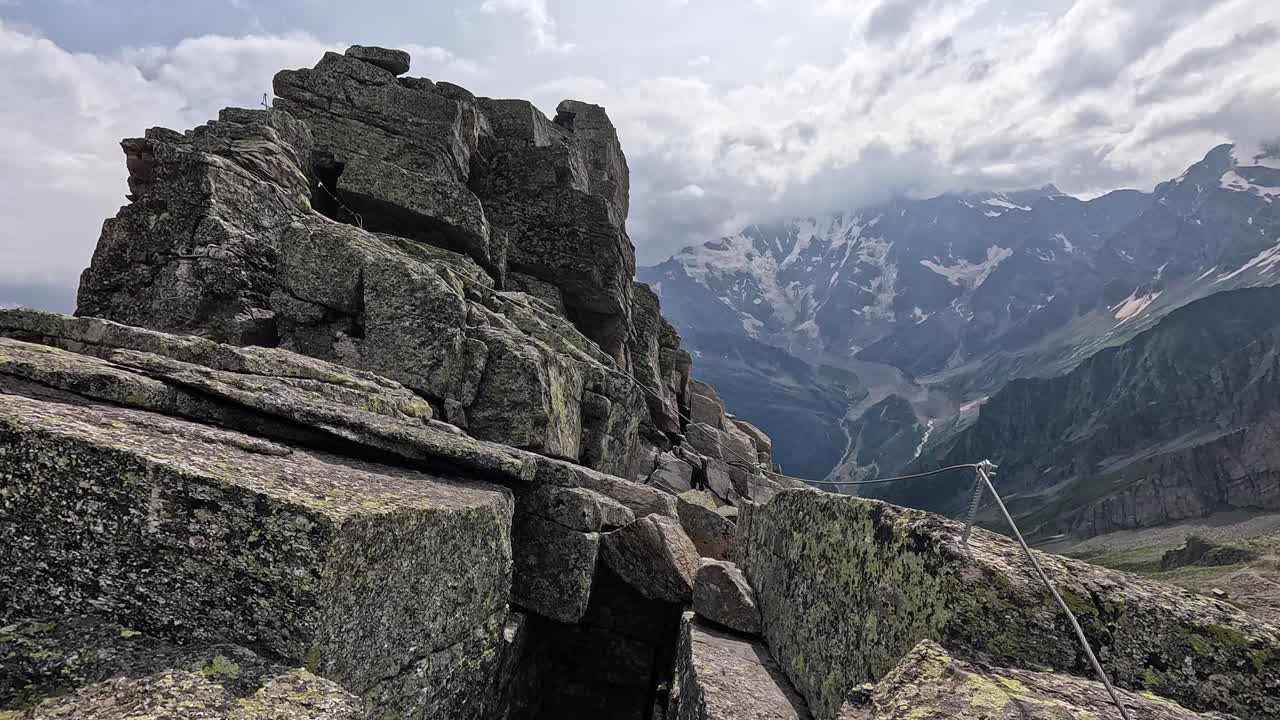 Steep rocky ledge with safety cable overlooking Monte Rosa and deep alpine valley near Macugnaga, Italy.