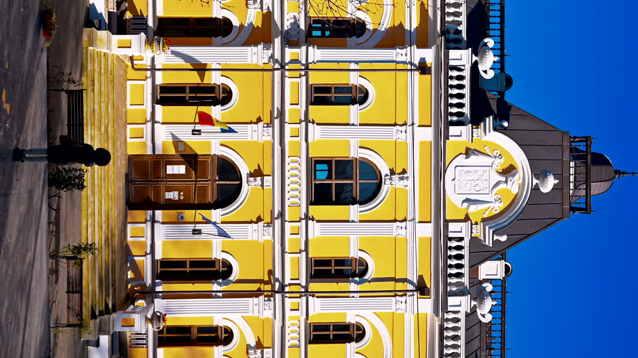 Beautiful historic building with yellow facade and intricate details stands against a clear blue sky. Sunlight highlights its architectural features, attracting visitors