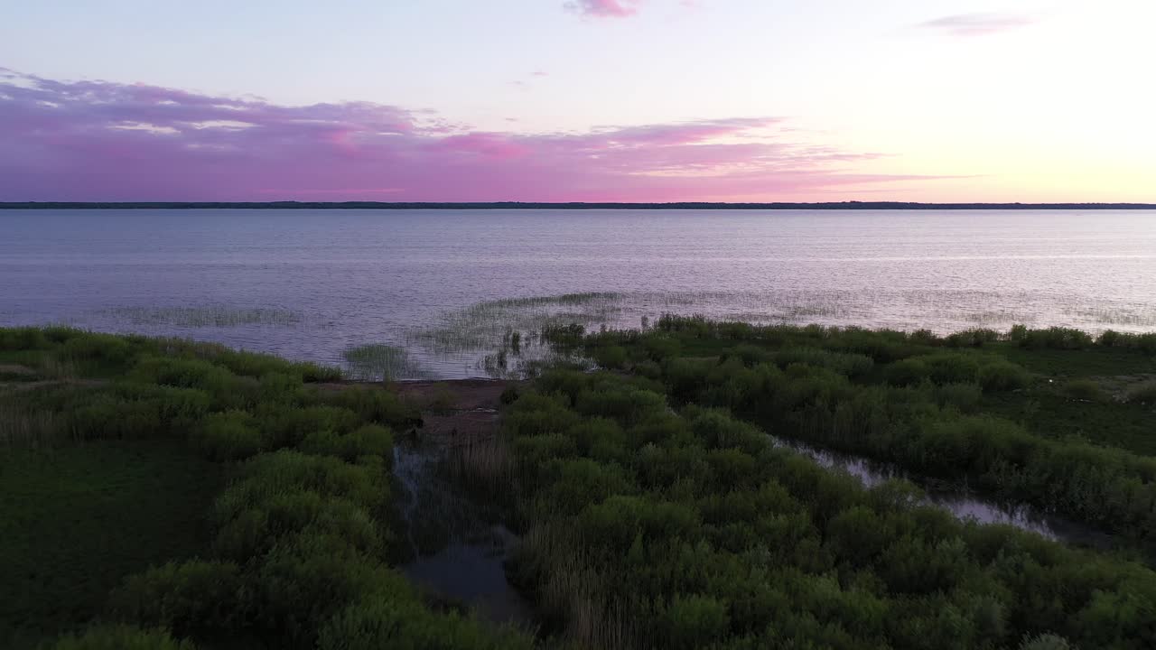 vista aérea de la costa del pantano de humedales volando a través del océano tranquilo bajo el horizonte de la puesta de sol púrpura