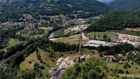 cross stands at the peak of apuseni mountains with a view of the village and aries river in romania